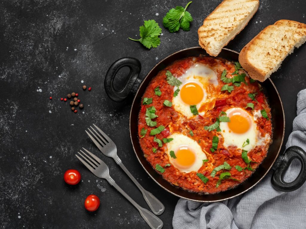 shakshuka,eggs,in,a,pan,with,toast,on,a,black